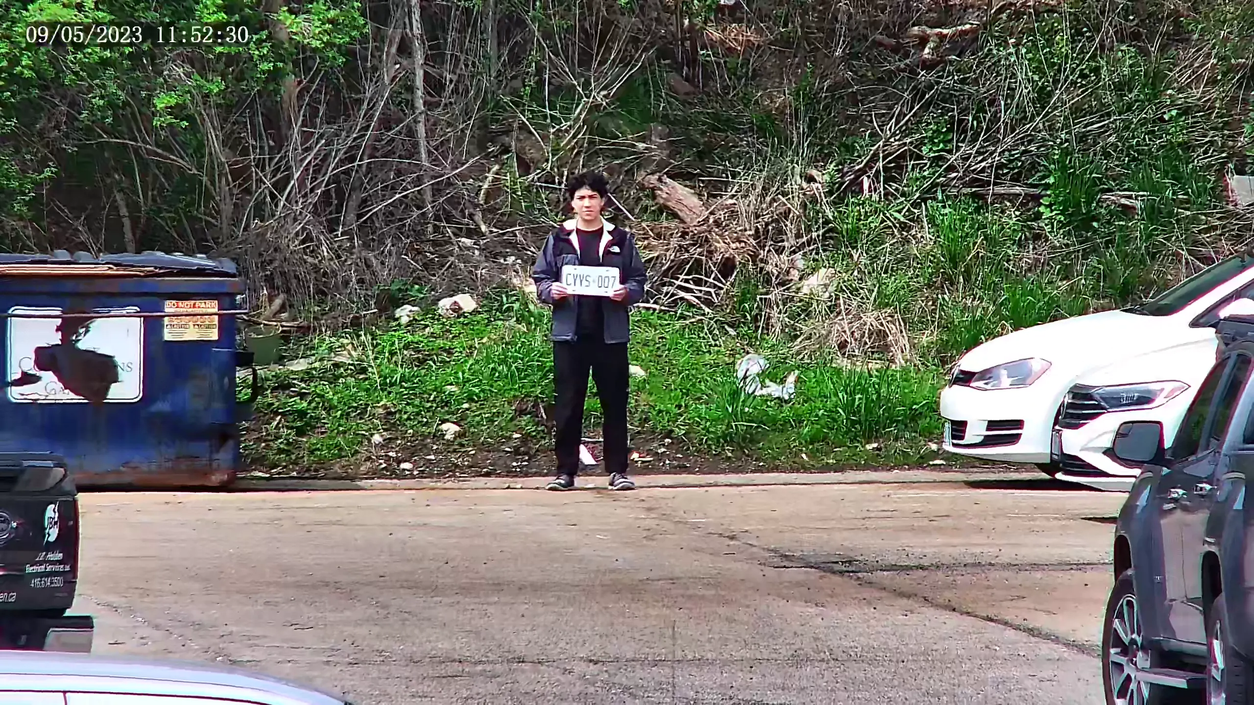 A fully zoomed in security camera showing a man with a grey jacket holding a license plate