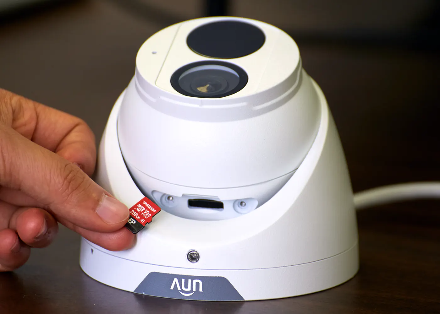 A hand holding a memory card, about to insert it into a security camera