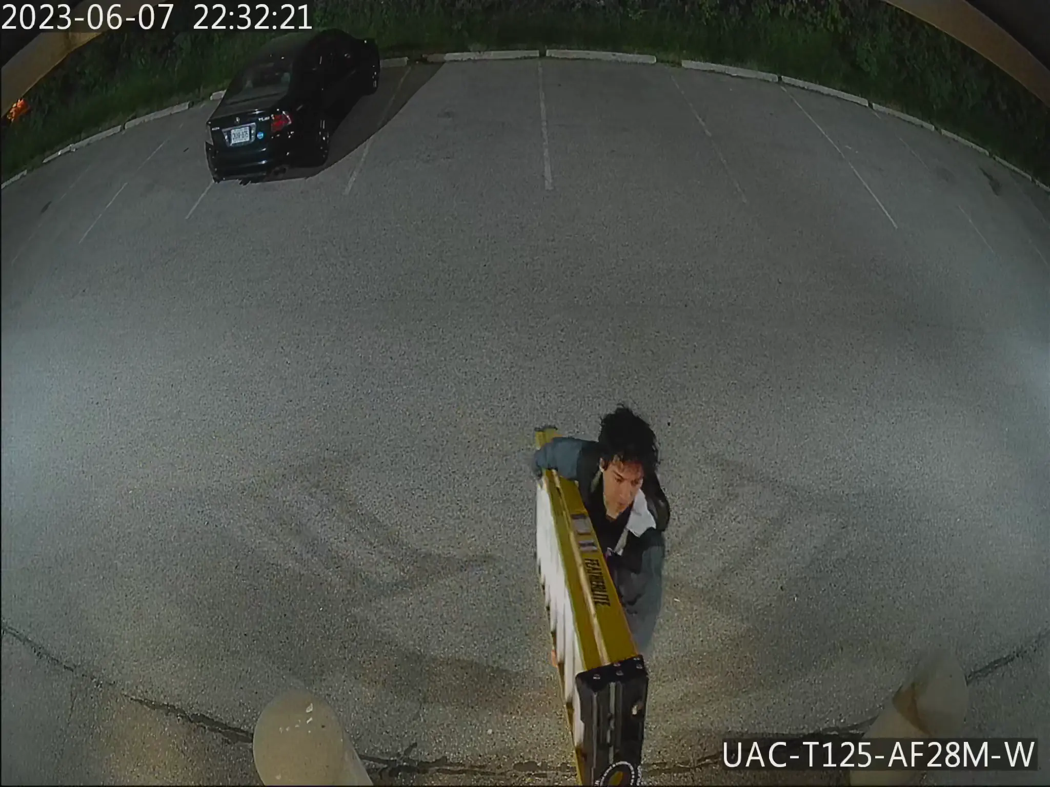 Security camera footage of a parking lot at night with a black car, and a person carrying a ladder