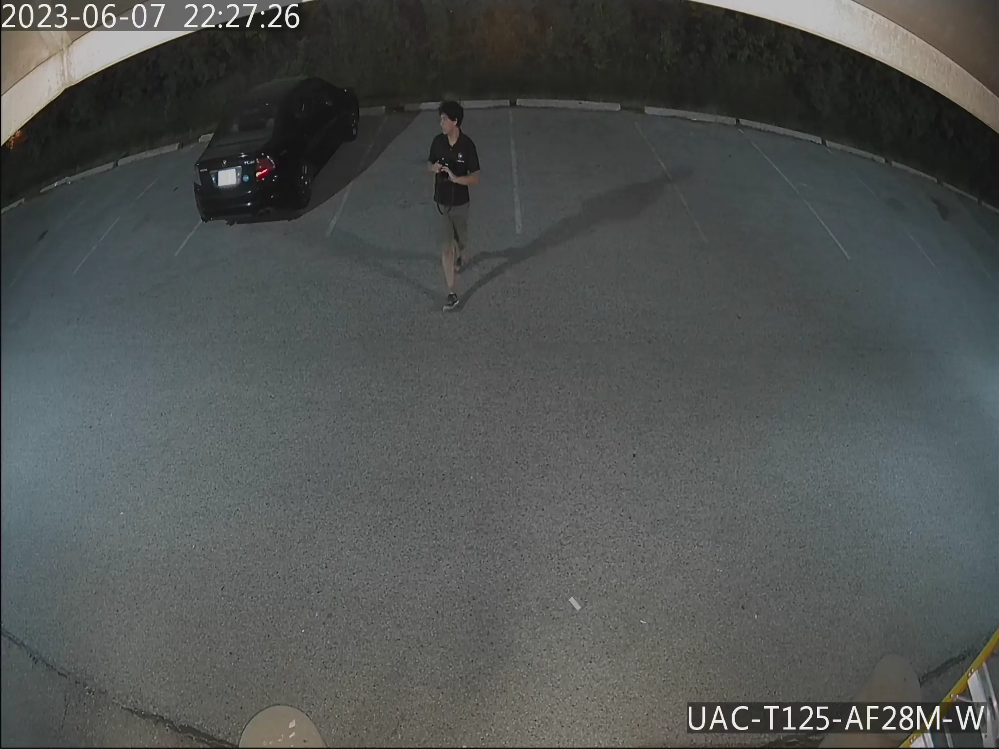 Security camera footage of a parking lot with a person standing beside a blackk car
