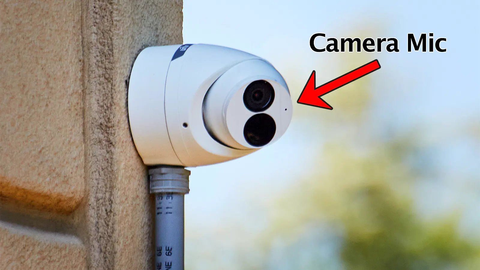 A security camera mounted outside on a brick wall. A conduit pipe is installed at the base of the camera.