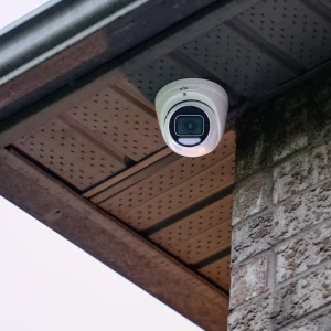 A white security camera installed underneath the soffit of a house with the sky in the background