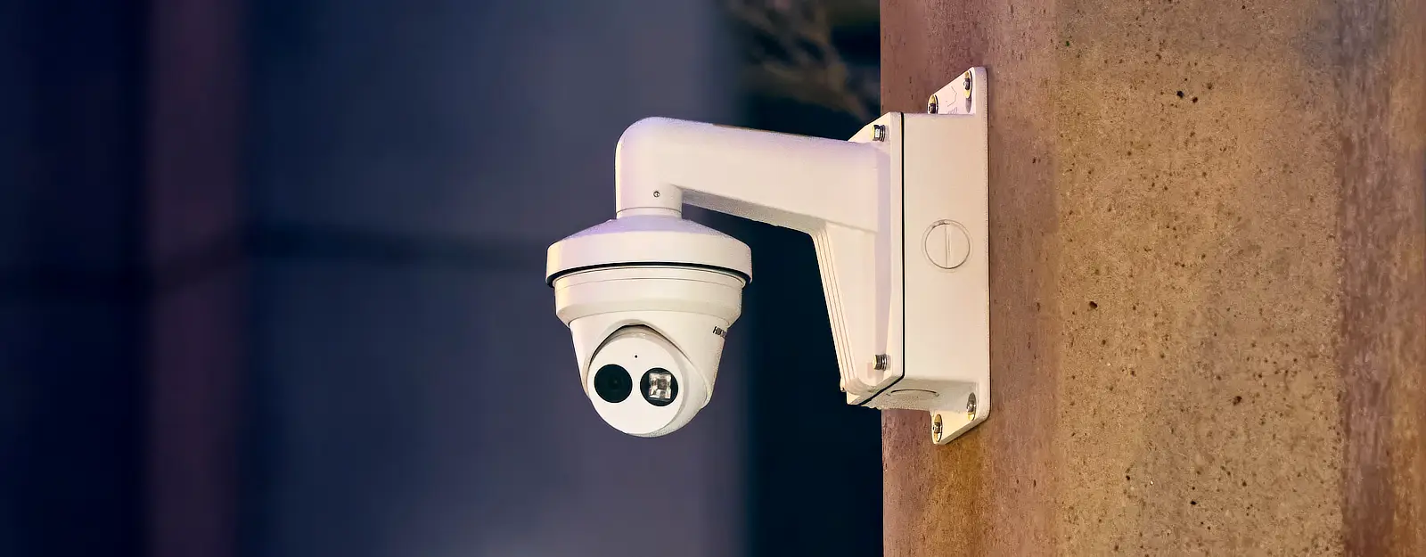 A Hikvsion security camera mounted on a metal wall bracket on a concrete wall