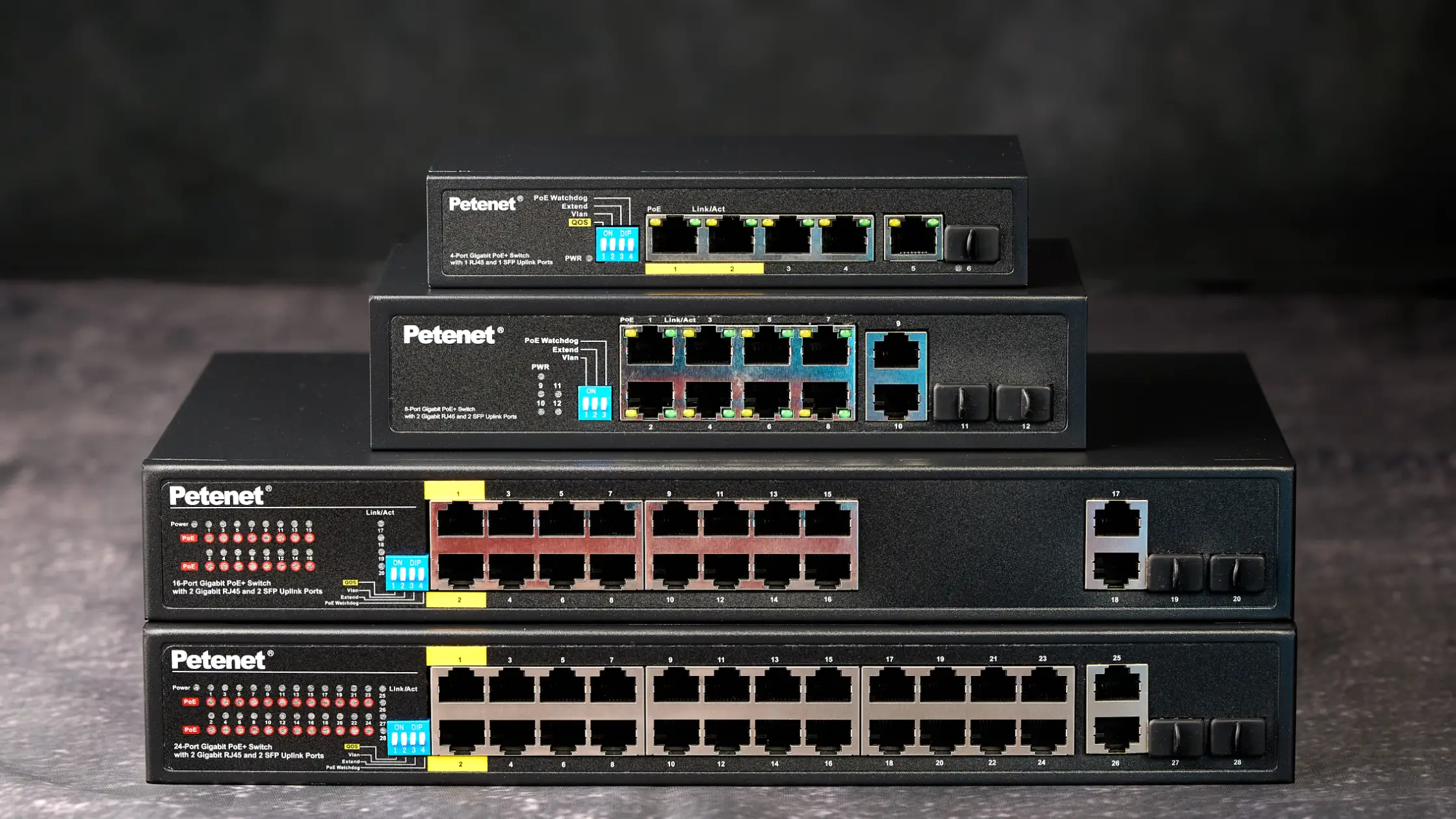 A stack of Petenet PoE switches are on a table with a dark stone background.