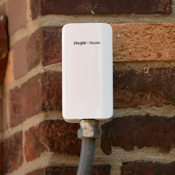 A wireless bridge made by Reyee installed using grey flexipipe and mounted on a brick wall