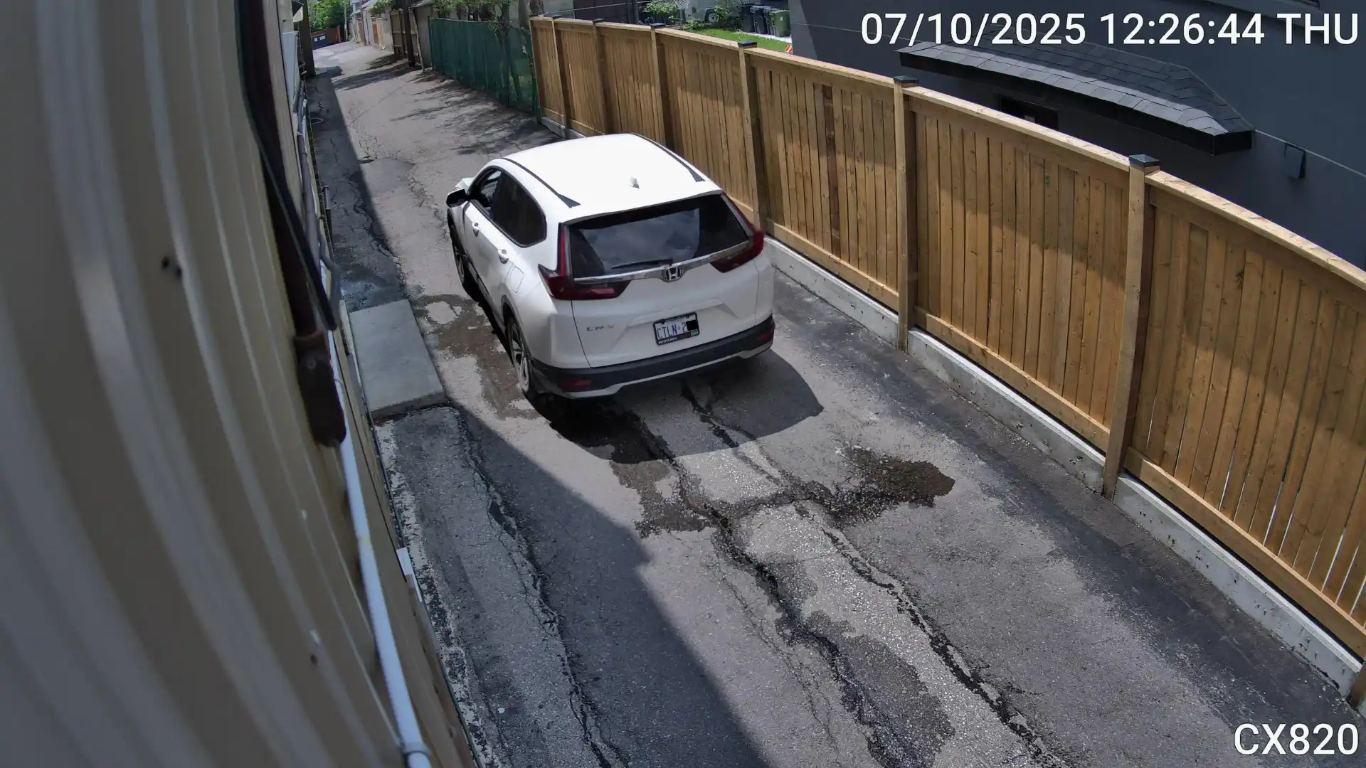 A snapshot taken by a security camera of a white van passing through a narrow driveway beside an apartment building