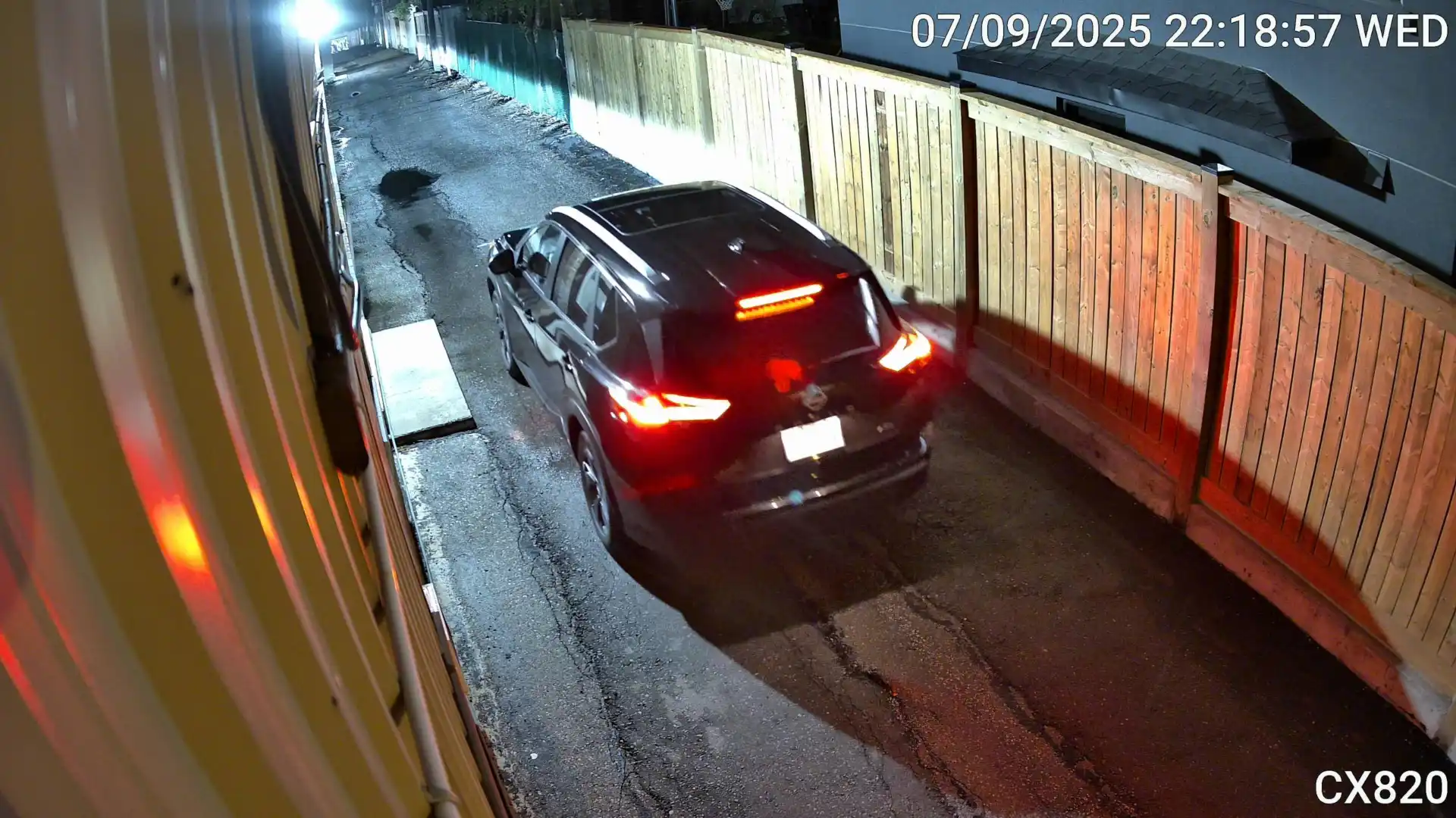 A snapshot from a Reolink security camera at night with a black van driving past. The license plate is obscured due to overexposure by the camera.