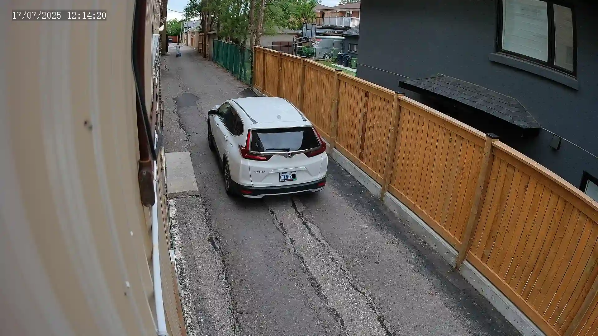 A snapshot captured by a Uniview security camera of a white Honda CRV driving past a narrow alleyway with the license plate clearly visible.
