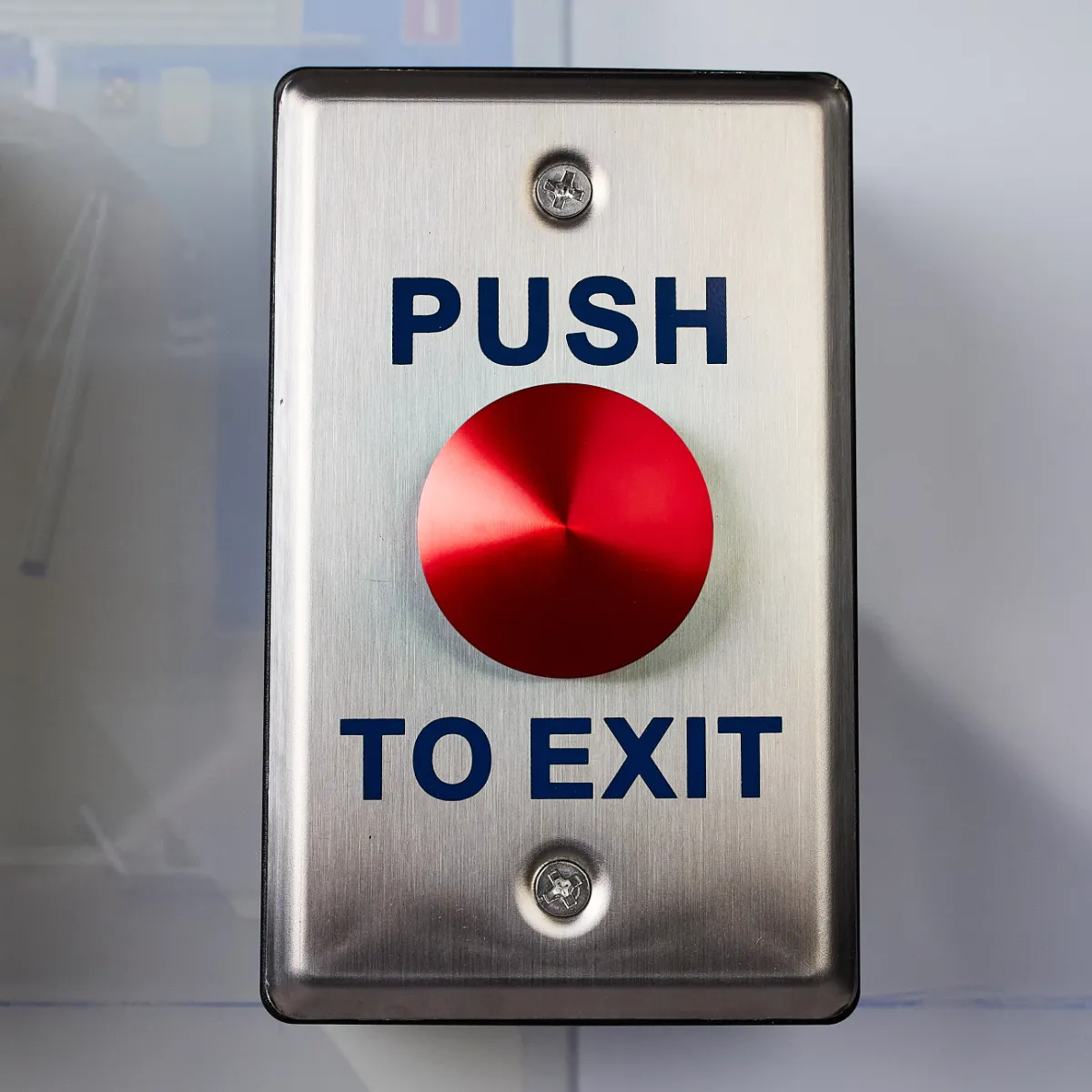 A metal push to exit switch with a large red button in the middle. The words Push to Exit is written above and below the button.