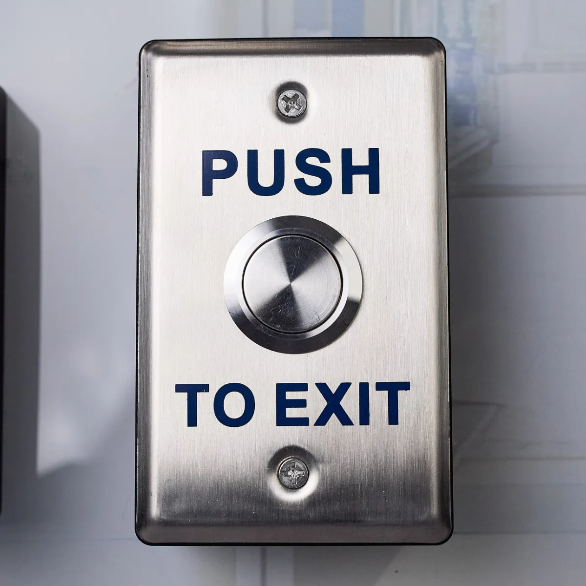 A metal push to exit switch with a large red button in the middle. The words Push to Exit is written above and below the button.