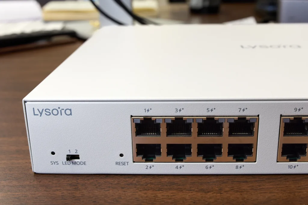 A white managed PoE switch from Lysora with a DIP switch for changing the LEDs between modes 1 and 2, plus a small hole for the reset button.