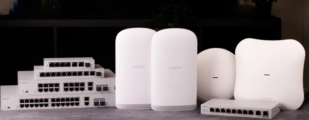 A collection of networking equipment from Lysora Networks on a table, including managed switches, wireless bridges, and access points.