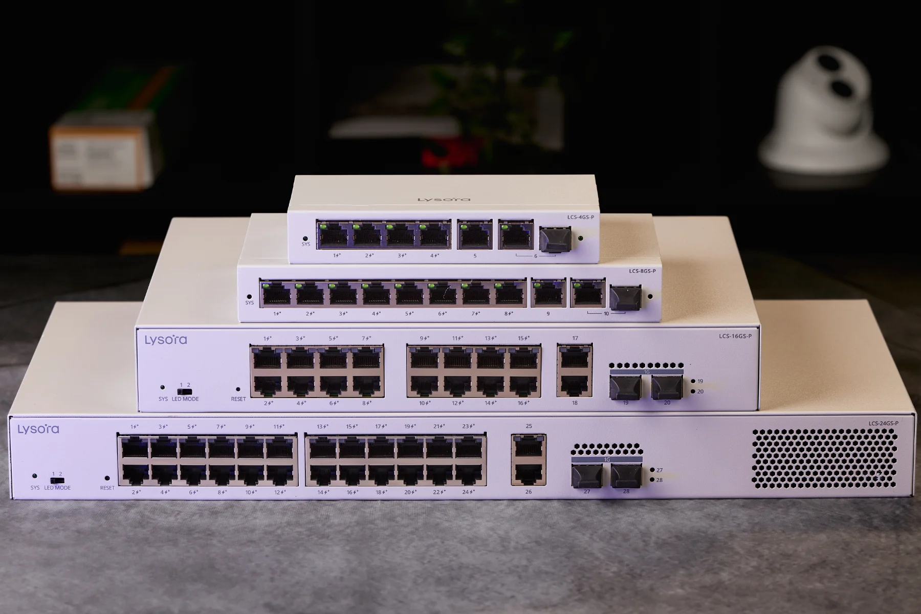 A stack of managed PoE switches on a table, ranging from 4-port at the top to 24-port at the bottom.