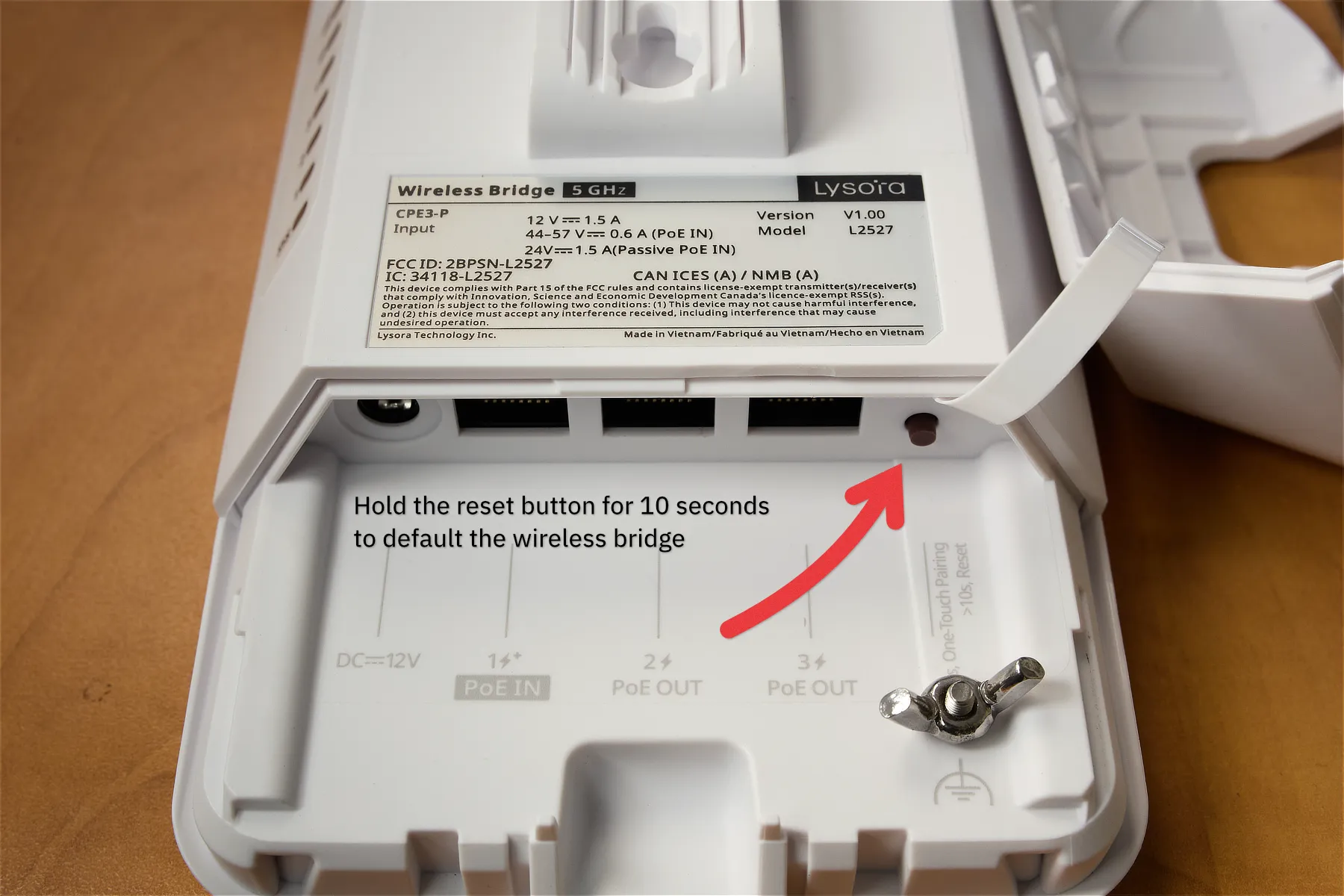 The bottom of a Lysora CPE3-P wireless bridge, with an arrow pointing to the brown reset button, along with text saying that you need to hold it down for 10 seconds to fully reset the bridge.
