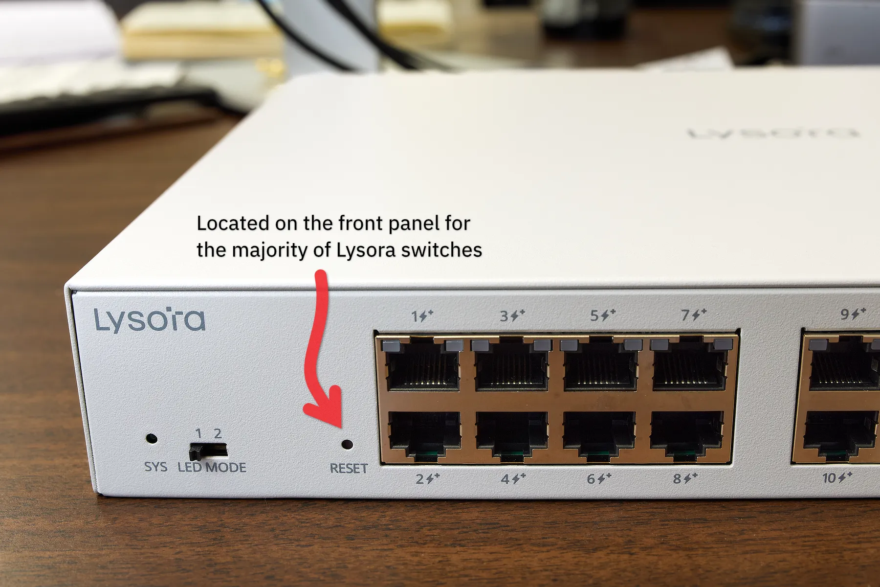 A close-up view of a Lysora 16-port network switch, with an arrow pointing to the reset button, which is located on the front panel at the left side.