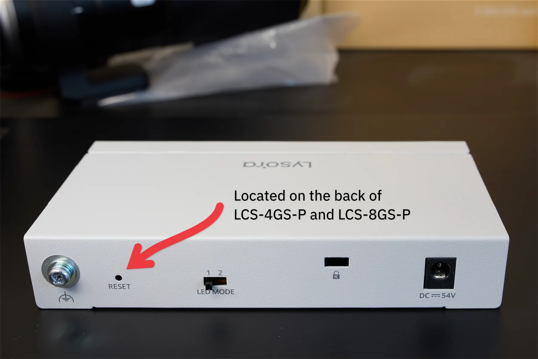 The rear panel of a white Lysora 4-port PoE switch with an arrow pointing to the reset button, which is on the left side.