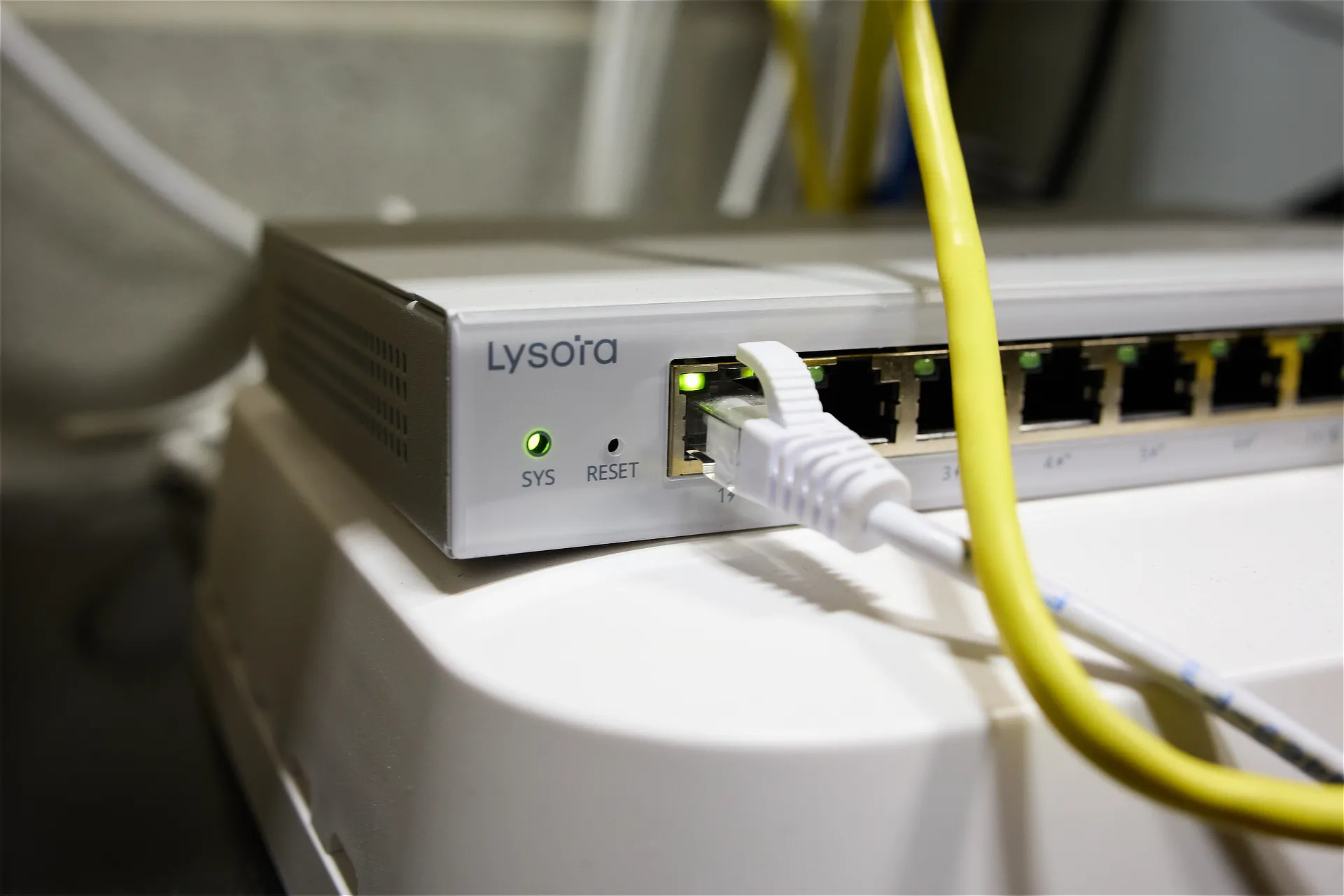 A Lysora router connected to the internet modem using a white cable. A yellow cable runs above the router, connecting to an unknown device out of frame.